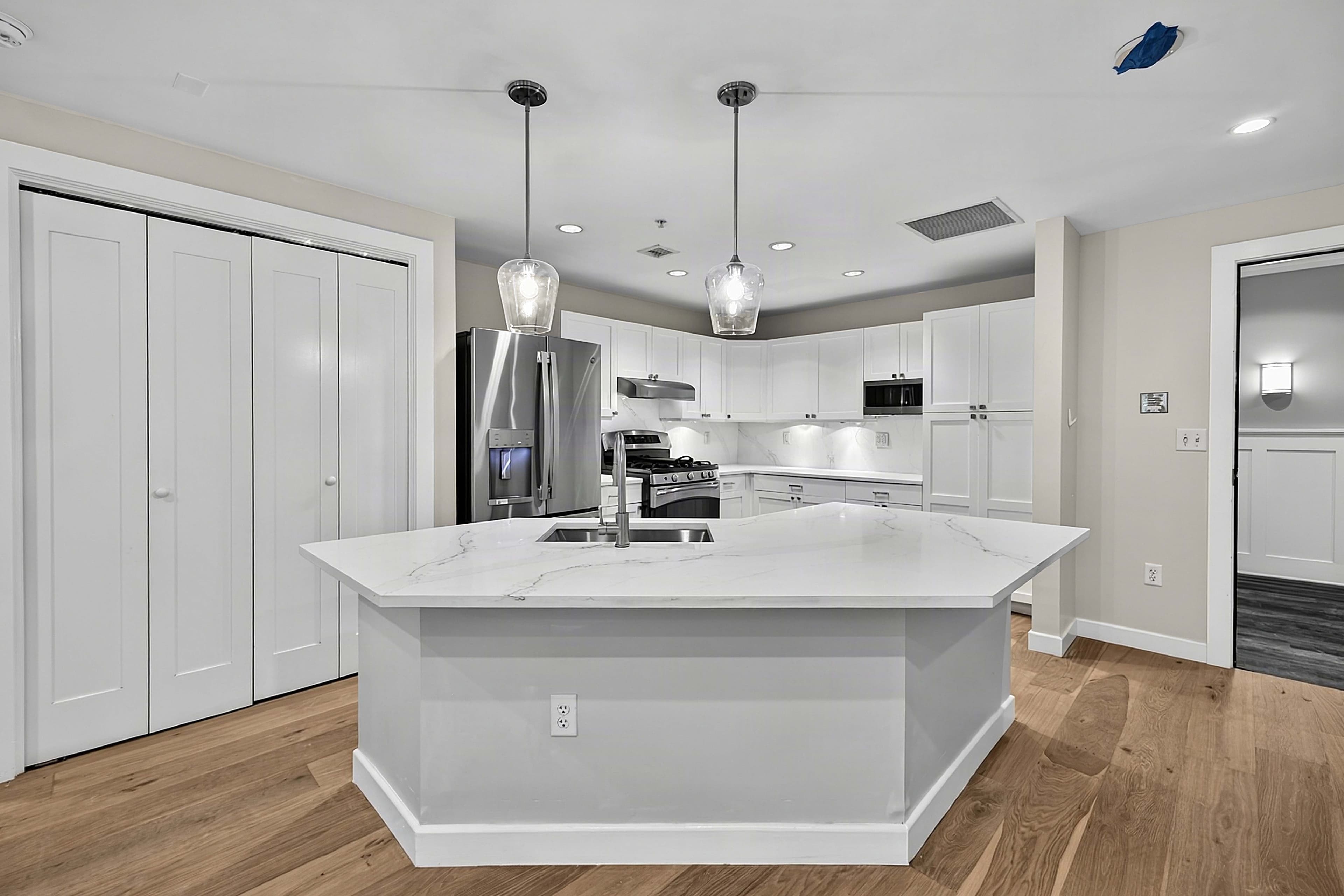 Angled view of the kitchen island, pendant lights, and white cabinets